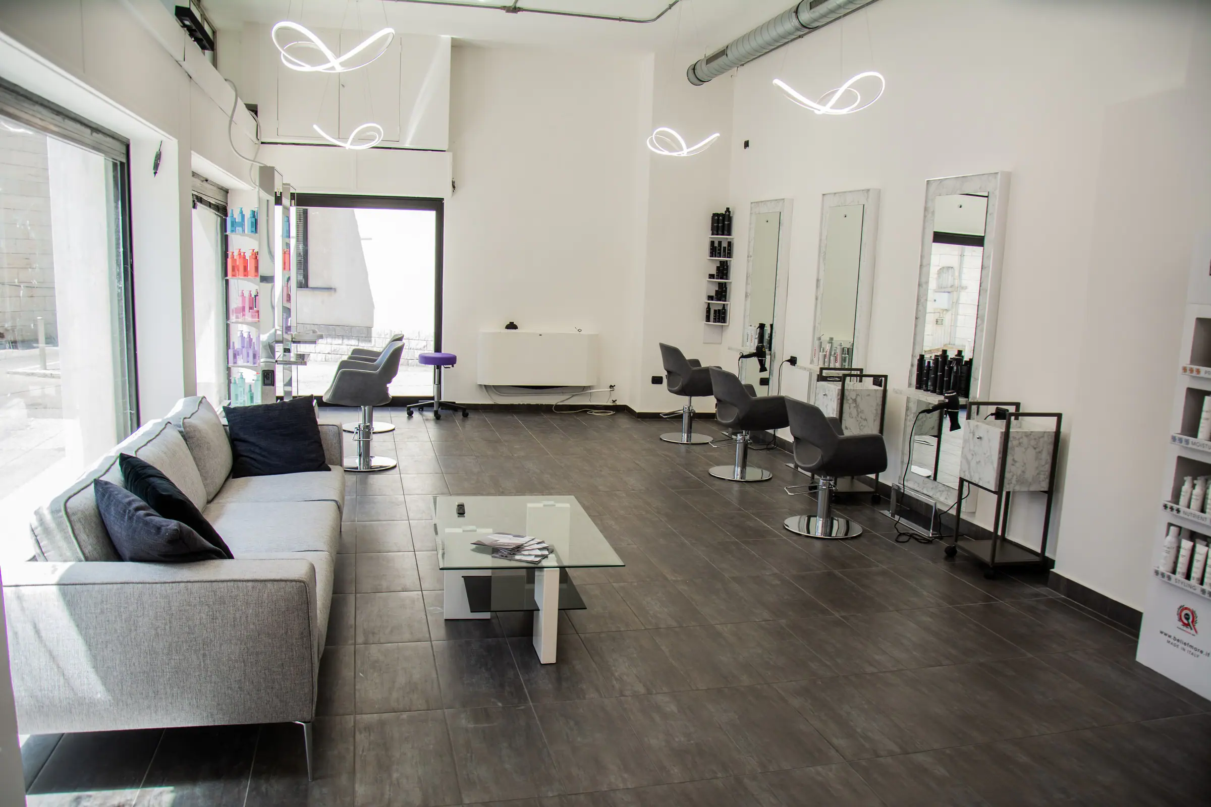Interno del salone con divano, postazioni con specchi e sedie grigie